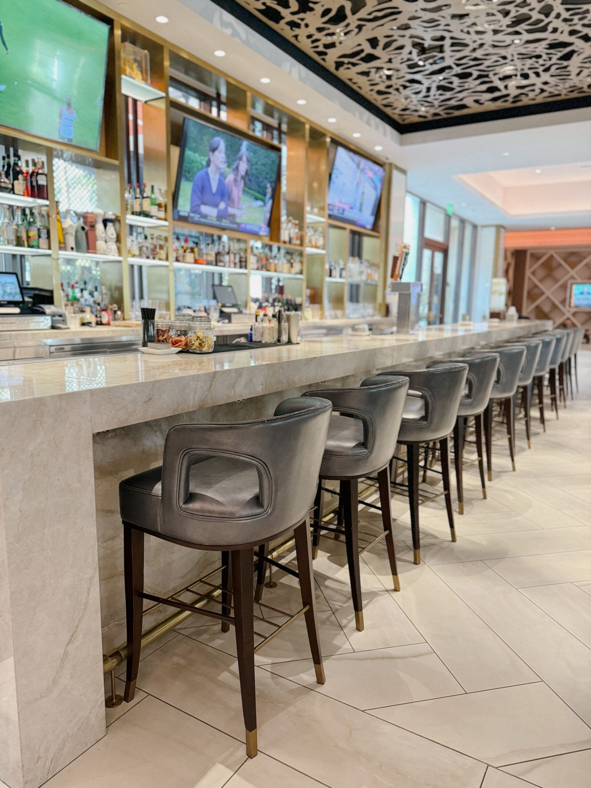 Bar with high-top seating, marble counter, and TV screens